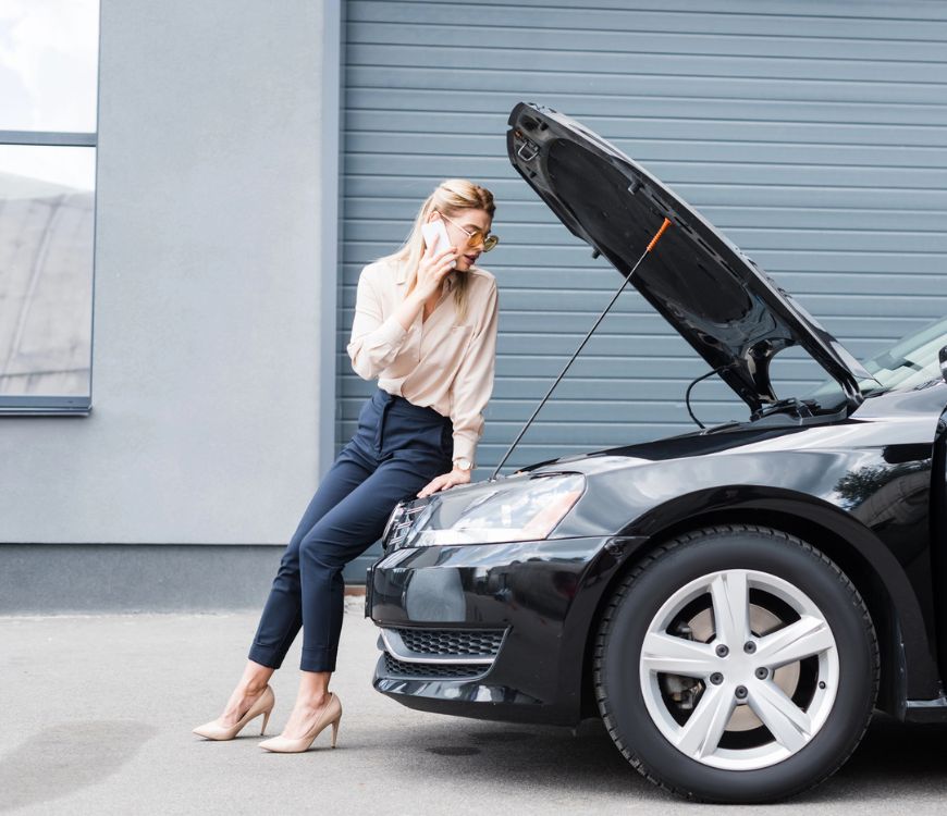 Businesswoman talking on smartphone while standing near broken auto