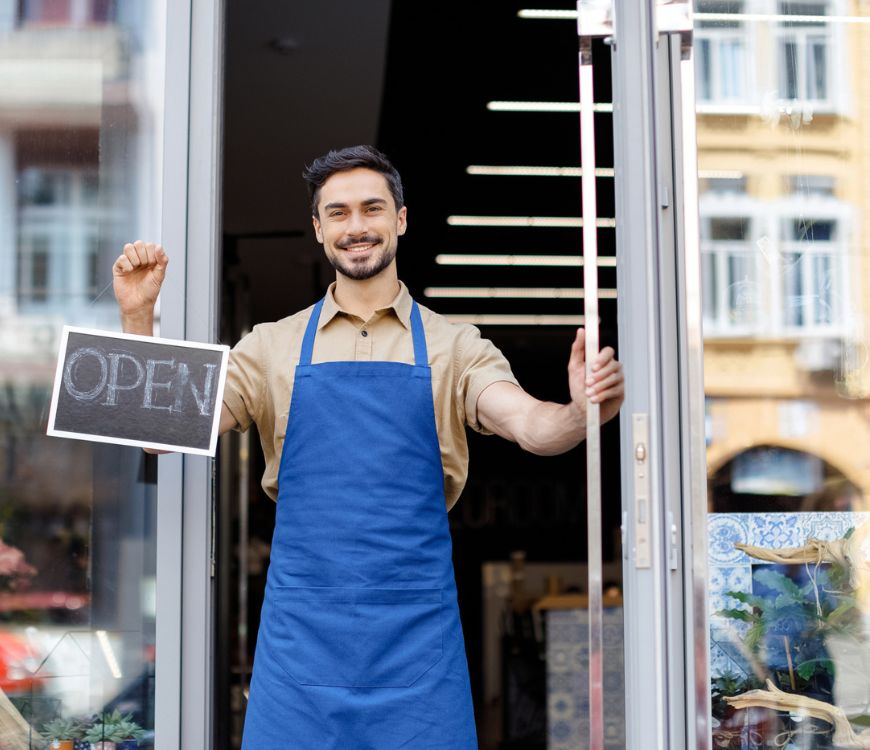 Small business owner in Sandy, UT standing in front of a store with an open sign